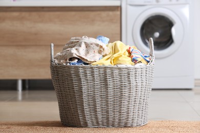 Photo of Wicker basket with dirty clothes on floor in laundry room