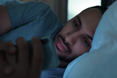 Photo of Young man using smartphone in bed at night, closeup. Internet addiction