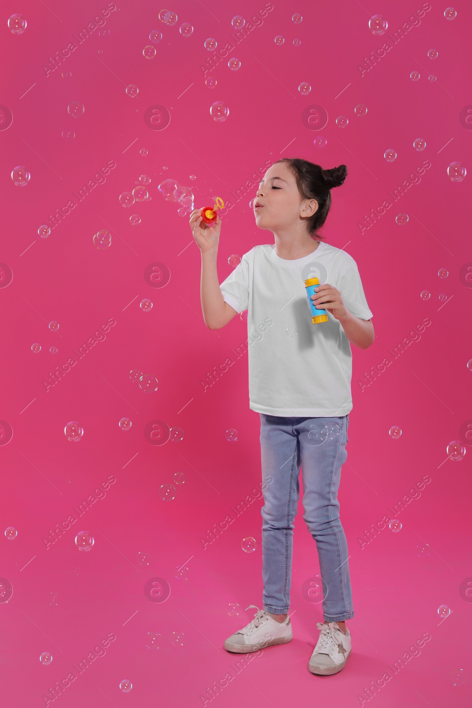 Photo of Little girl blowing soap bubbles on pink background