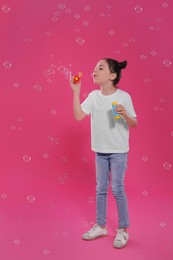 Little girl blowing soap bubbles on pink background