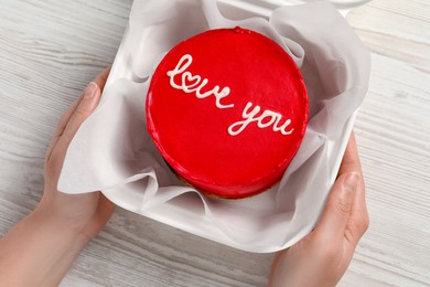 Woman holding takeaway box with bento cake at white wooden table, top view. St. Valentine's day surprise