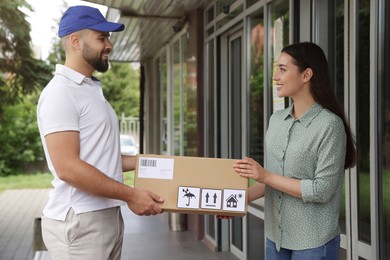 Photo of Woman receiving parcel from courier outdoors. Delivery service