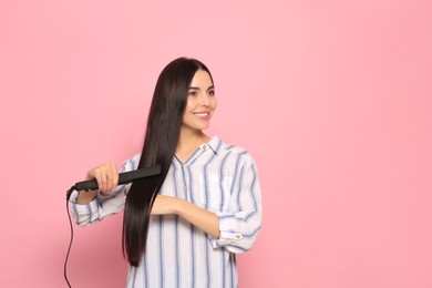 Beautiful happy woman using hair iron on pink background. Space for text