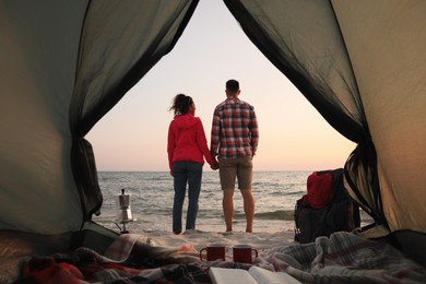 Photo of Couple near sea at sunset, view from camping tent