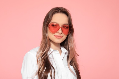 Portrait of beautiful young woman with heart shaped sunglasses on color background