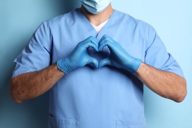 Photo of Doctor making heart with hands on light blue background, closeup
