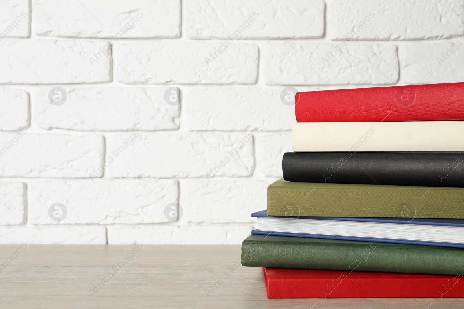 Photo of Stack of hardcover books on grey table near white brick wall, space for text