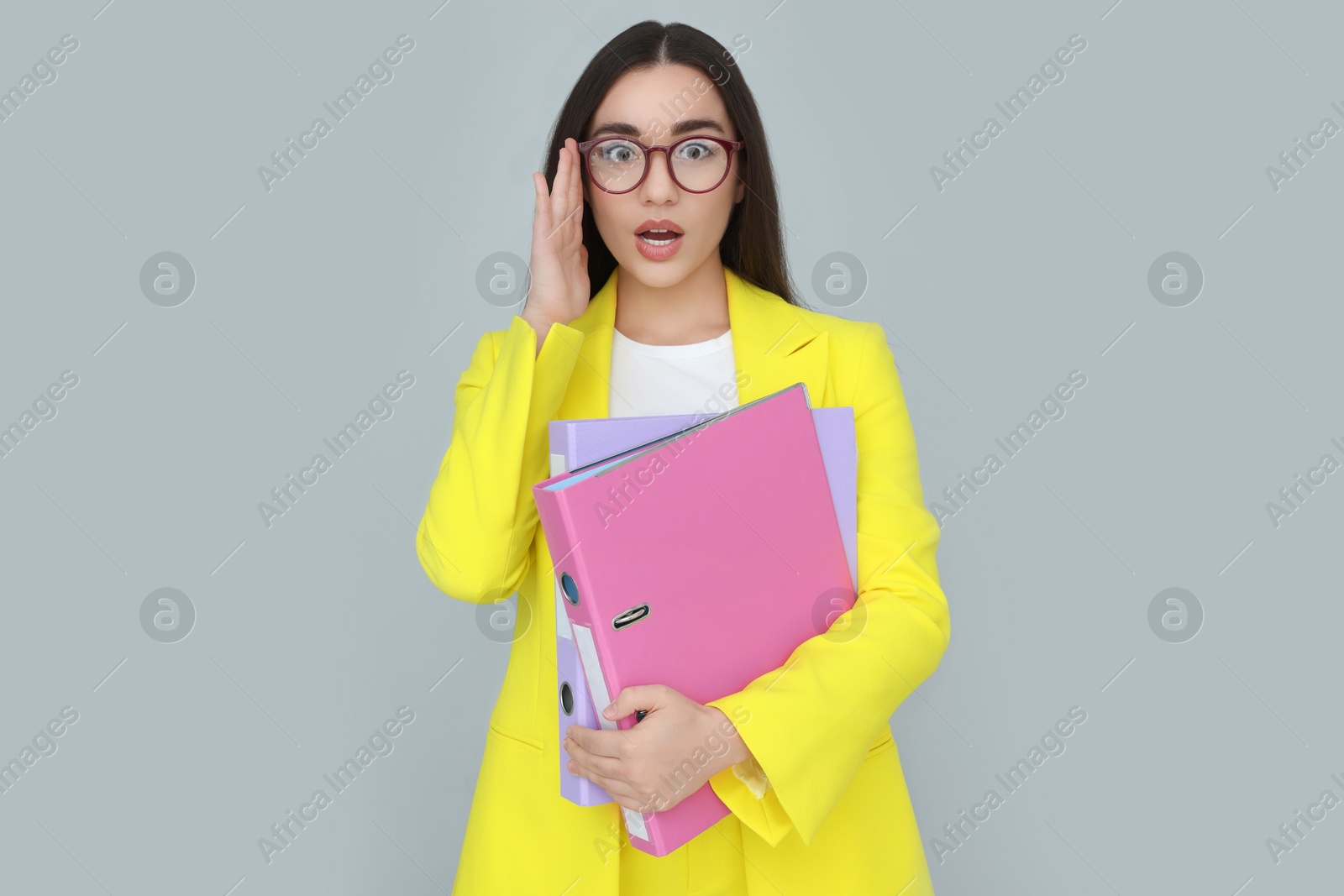 Photo of Young female intern with eyeglasses and folders on grey background