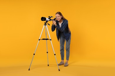 Photo of Young astronomer looking at stars through telescope on orange background