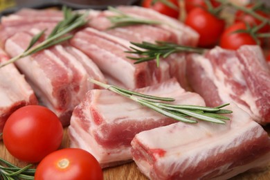 Photo of Cut raw pork ribs with rosemary and tomatoes on wooden board, closeup