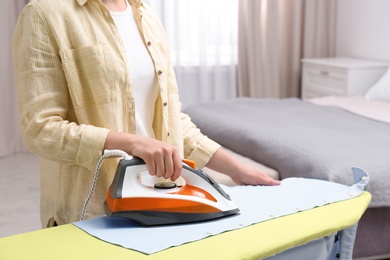 Photo of Woman ironing clothes on board in bedroom, closeup with space for text. Laundry day