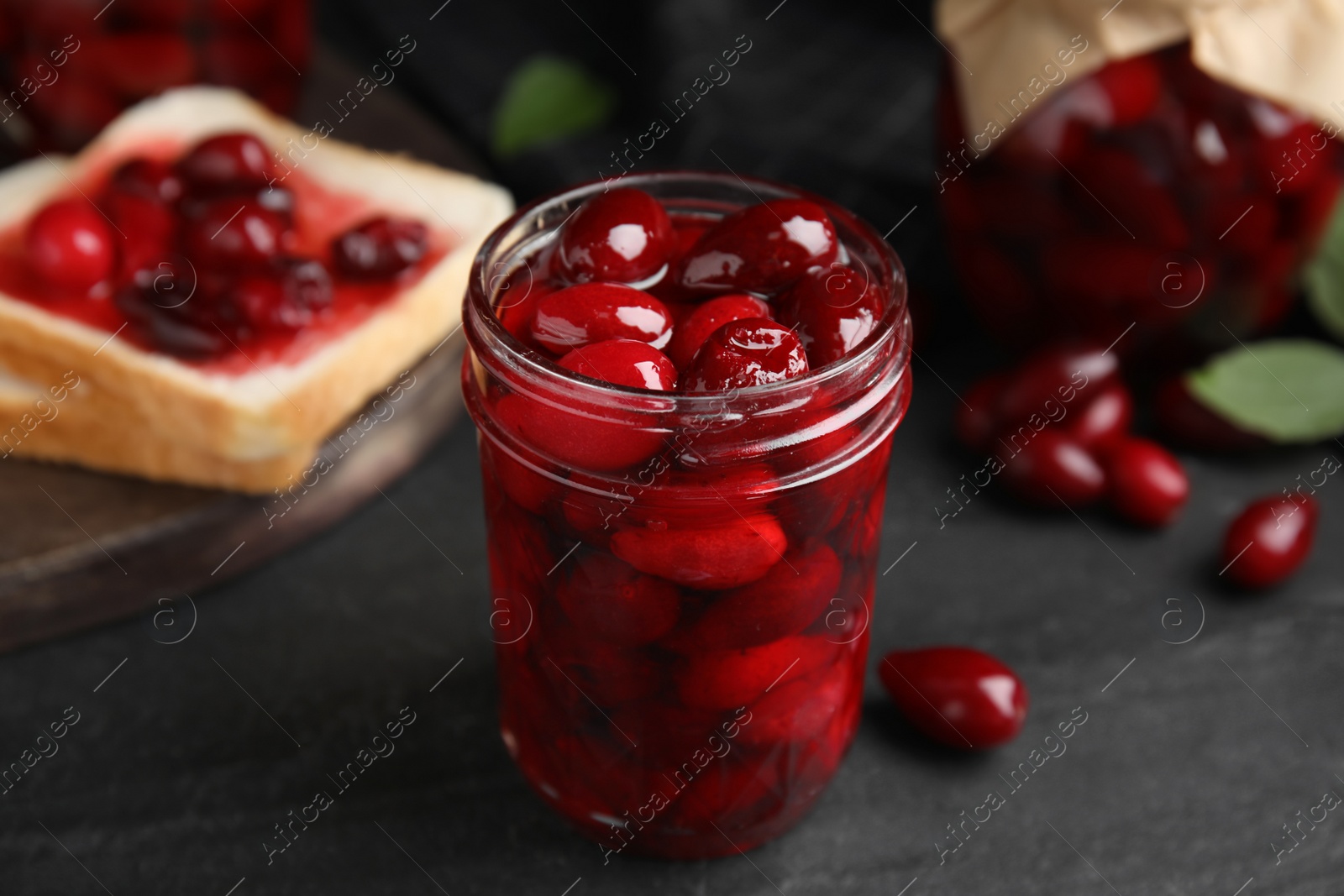 Photo of Delicious dogwood jam with berries in glass jar on black table, closeup