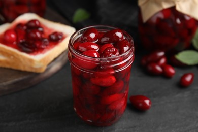 Photo of Delicious dogwood jam with berries in glass jar on black table, closeup