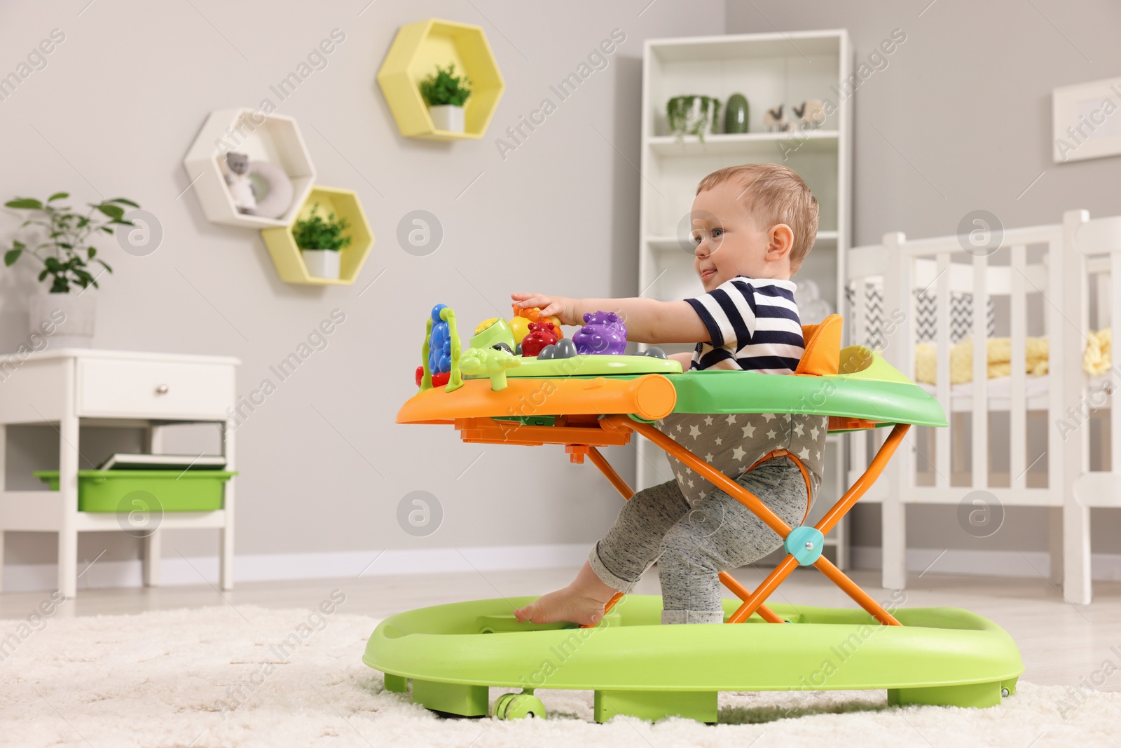 Photo of Cute baby making first steps with toy walker at home, space for text