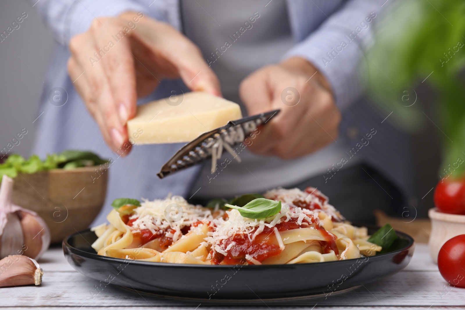 Photo of Woman grating parmesan cheese onto delicious pasta at wooden table, closeup