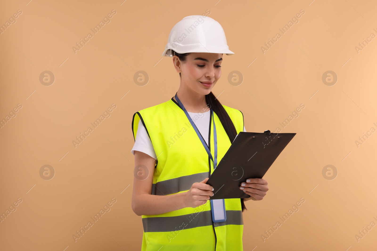 Photo of Engineer in hard hat holding clipboard on beige background