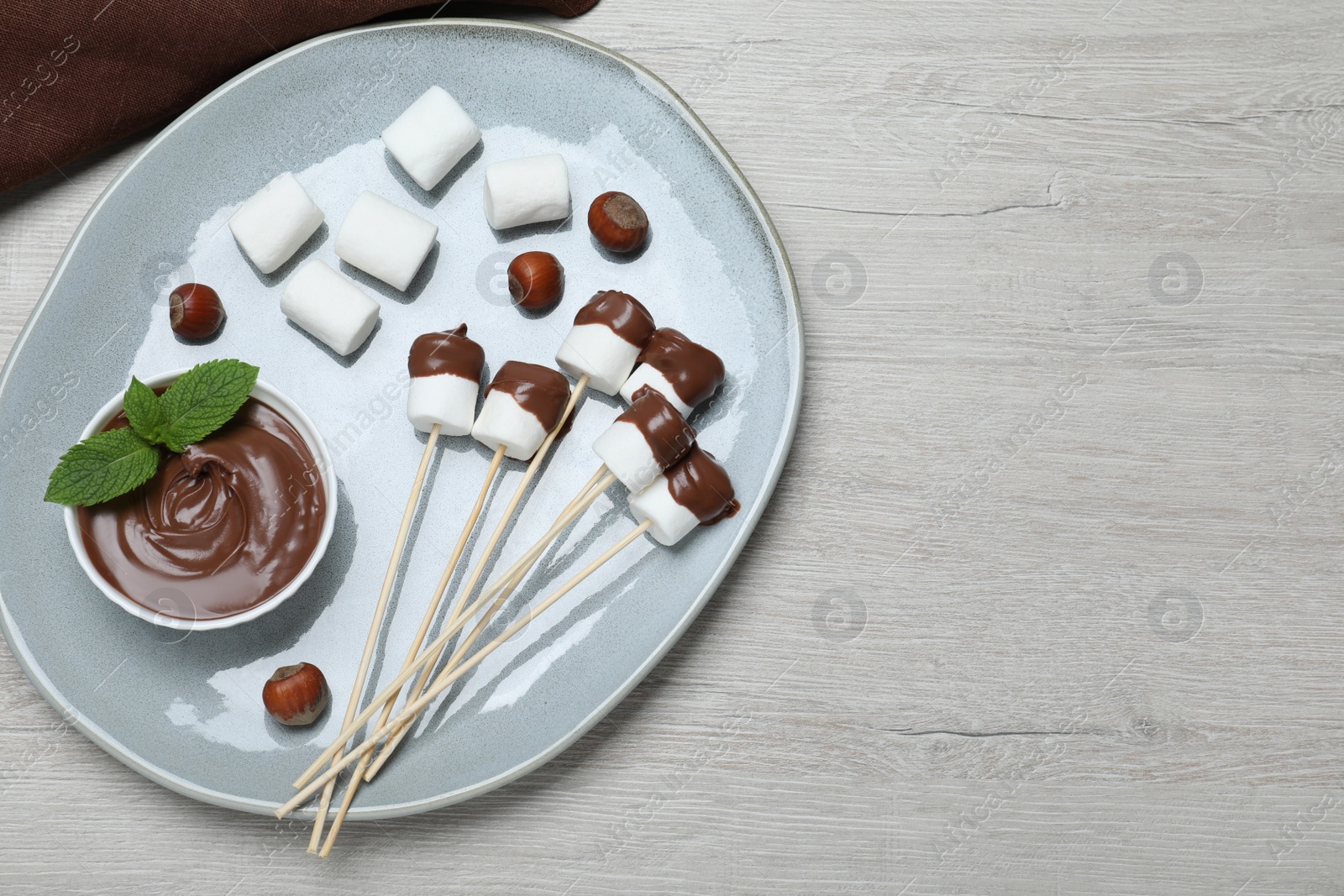 Photo of Tasty marshmallows dipped into chocolate on white wooden table, top view. Space for text