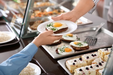Photo of Woman giving plate with healthy food to boy in school canteen, closeup