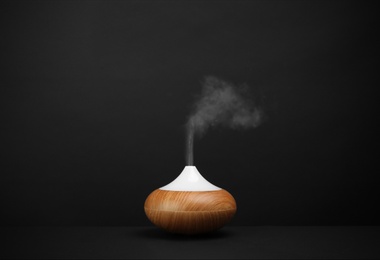 Photo of Modern essential oil diffuser on black background. Space for text