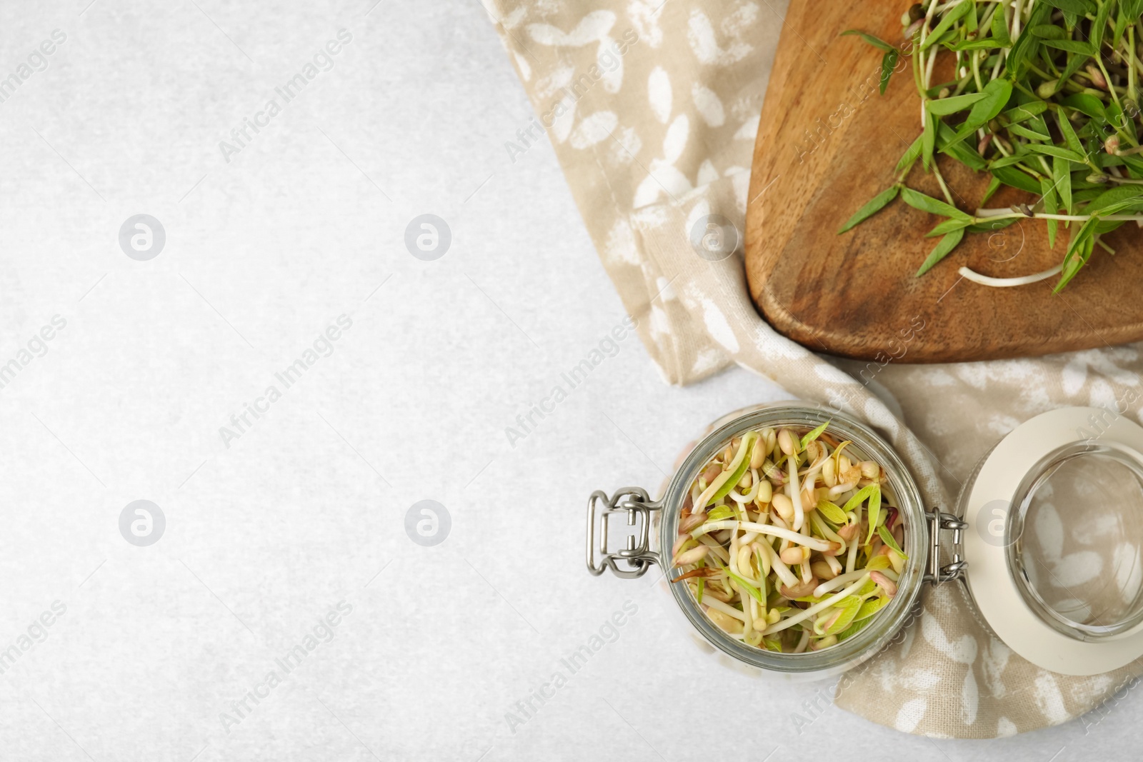 Photo of Mung bean sprouts in glass jar and wooden board on light table, flat lay. Space for text