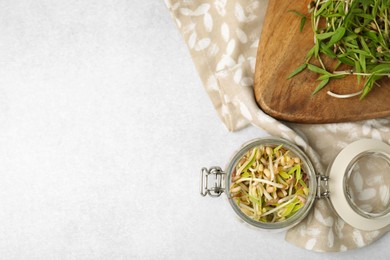 Photo of Mung bean sprouts in glass jar and wooden board on light table, flat lay. Space for text