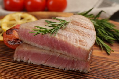 Photo of Pieces of delicious tuna steak with rosemary on wooden board, closeup