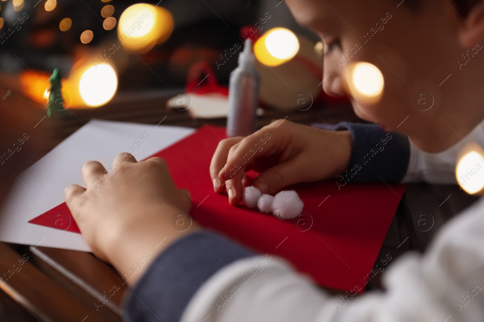 Photo of Little child making Christmas card at wooden table, closeup