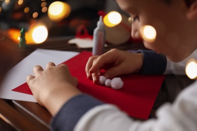 Little child making Christmas card at wooden table, closeup