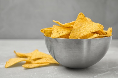 Photo of Metal bowl with tasty Mexican nachos chips on grey table, space for text