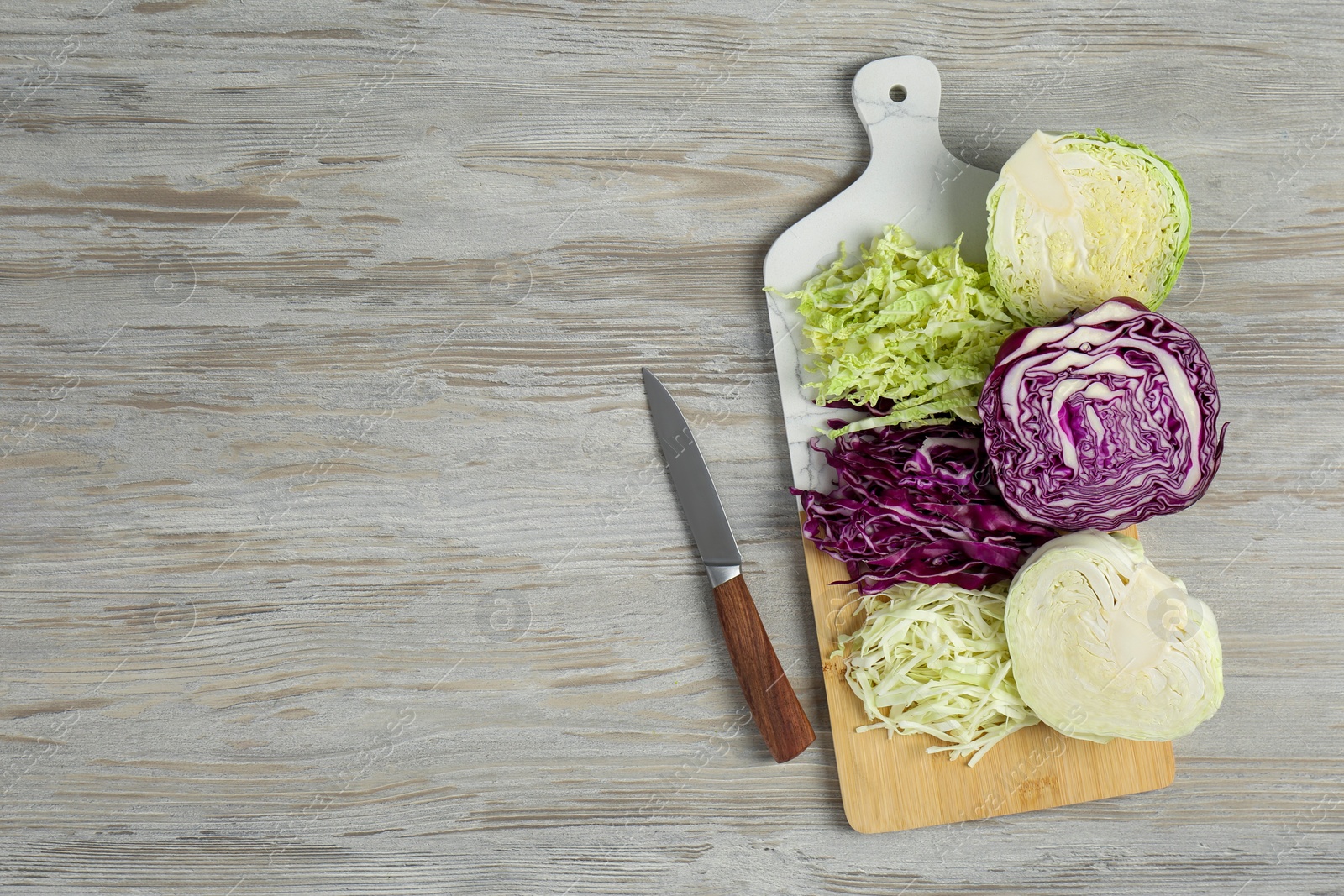 Photo of Different types of cut cabbage and knife on white wooden table, flat lay. Space for text