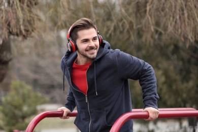 Young man with headphones listening to music and exercising on sports ground