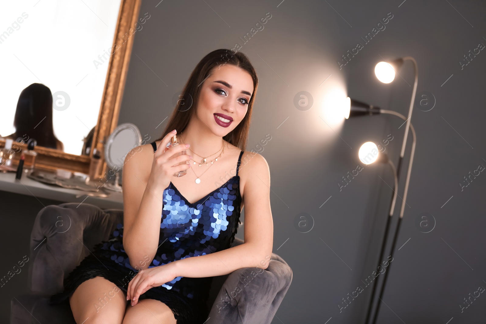 Photo of Portrait of beautiful woman with bright makeup applying perfume indoors