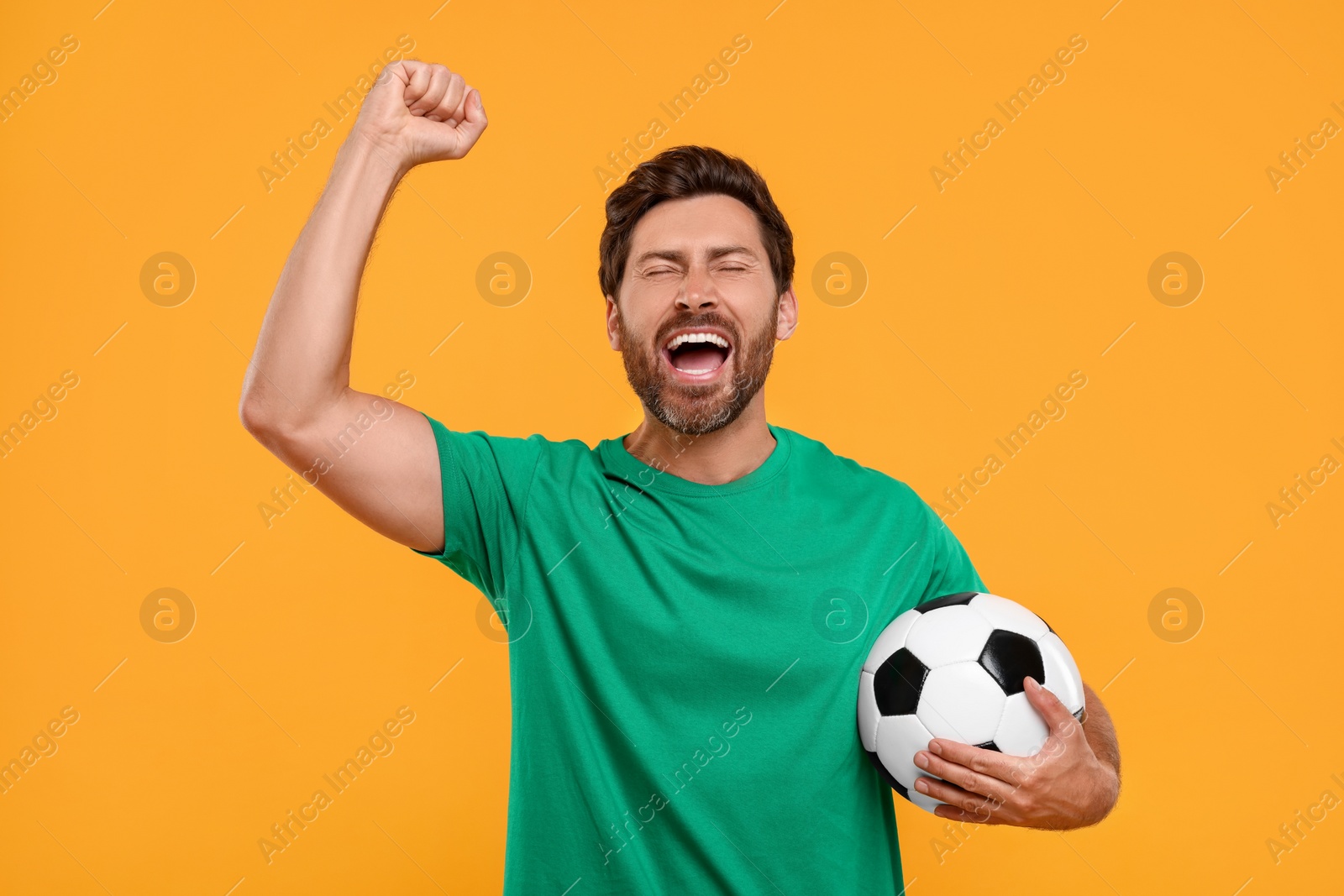 Photo of Emotional sports fan with soccer ball on orange background