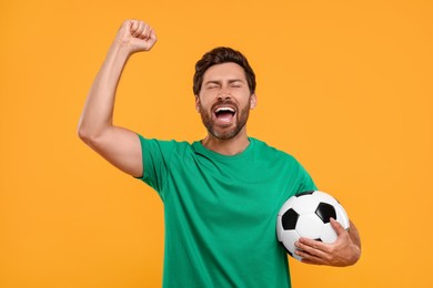 Emotional sports fan with soccer ball on orange background
