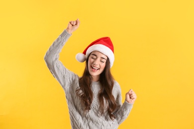 Beautiful woman wearing Santa Claus hat on yellow background