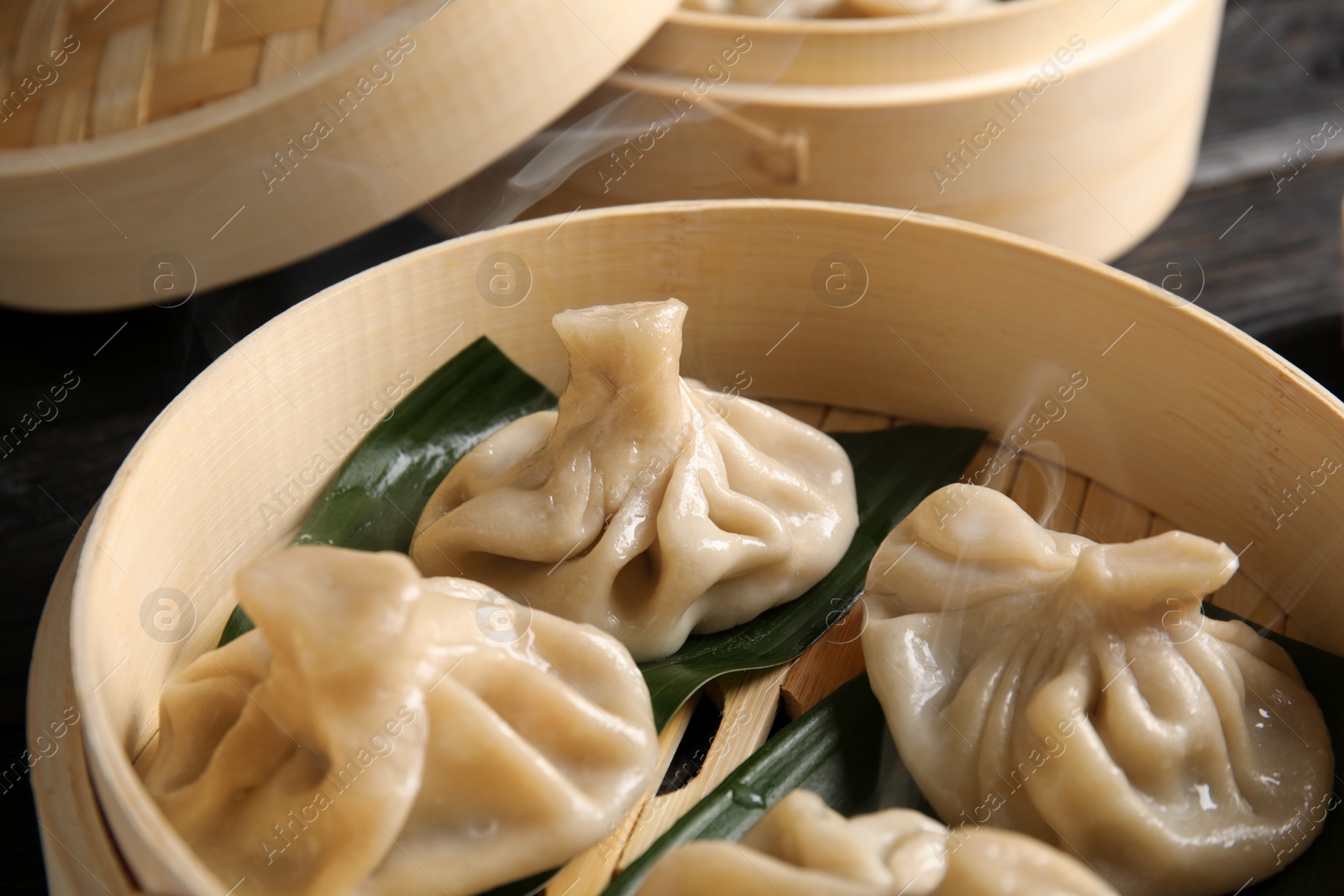 Photo of Bamboo steamer with leaves and tasty baozi dumplings on table, closeup