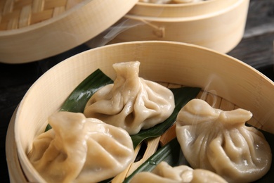 Bamboo steamer with leaves and tasty baozi dumplings on table, closeup