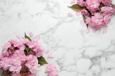 Photo of Beautiful sakura tree blossoms on white marble table, flat lay. Space for text