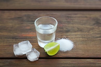 Photo of Mexican tequila shot with lime slice, ice cubes and salt on wooden table. Drink made from agave