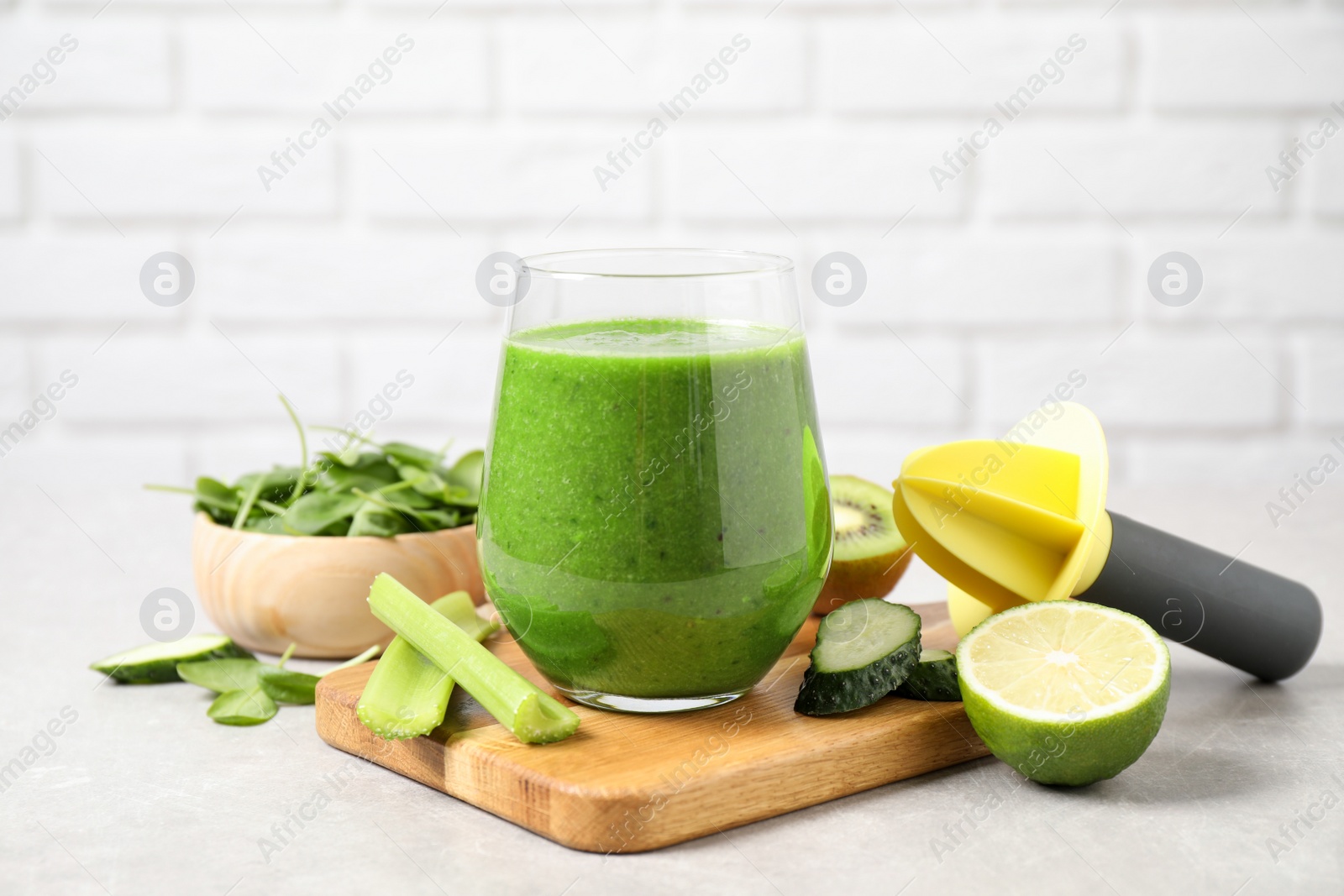 Photo of Delicious green juice and fresh ingredients on grey table against brick wall