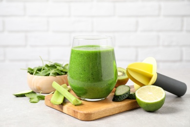 Photo of Delicious green juice and fresh ingredients on grey table against brick wall