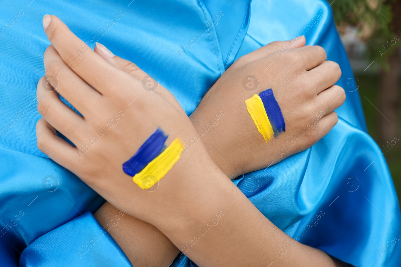 Photo of Woman with drawings of Ukrainian flag on hands outdoors, closeup