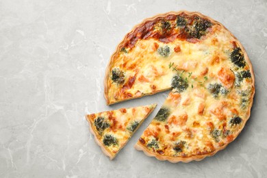 Photo of Delicious homemade quiche with salmon and broccoli on light gray marble table, flat lay. Space for text