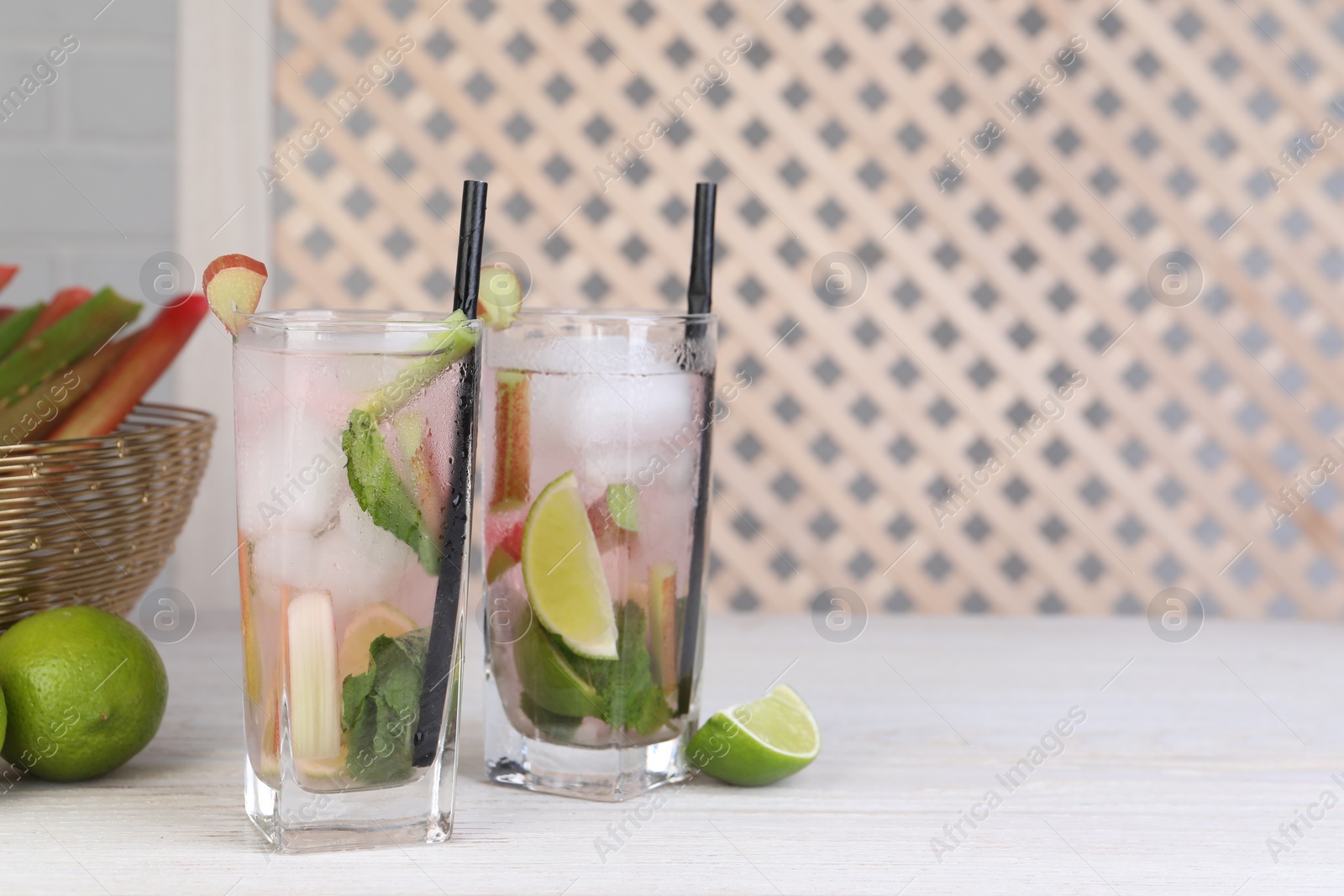 Photo of Tasty rhubarb cocktail with lime on white wooden table, space for text