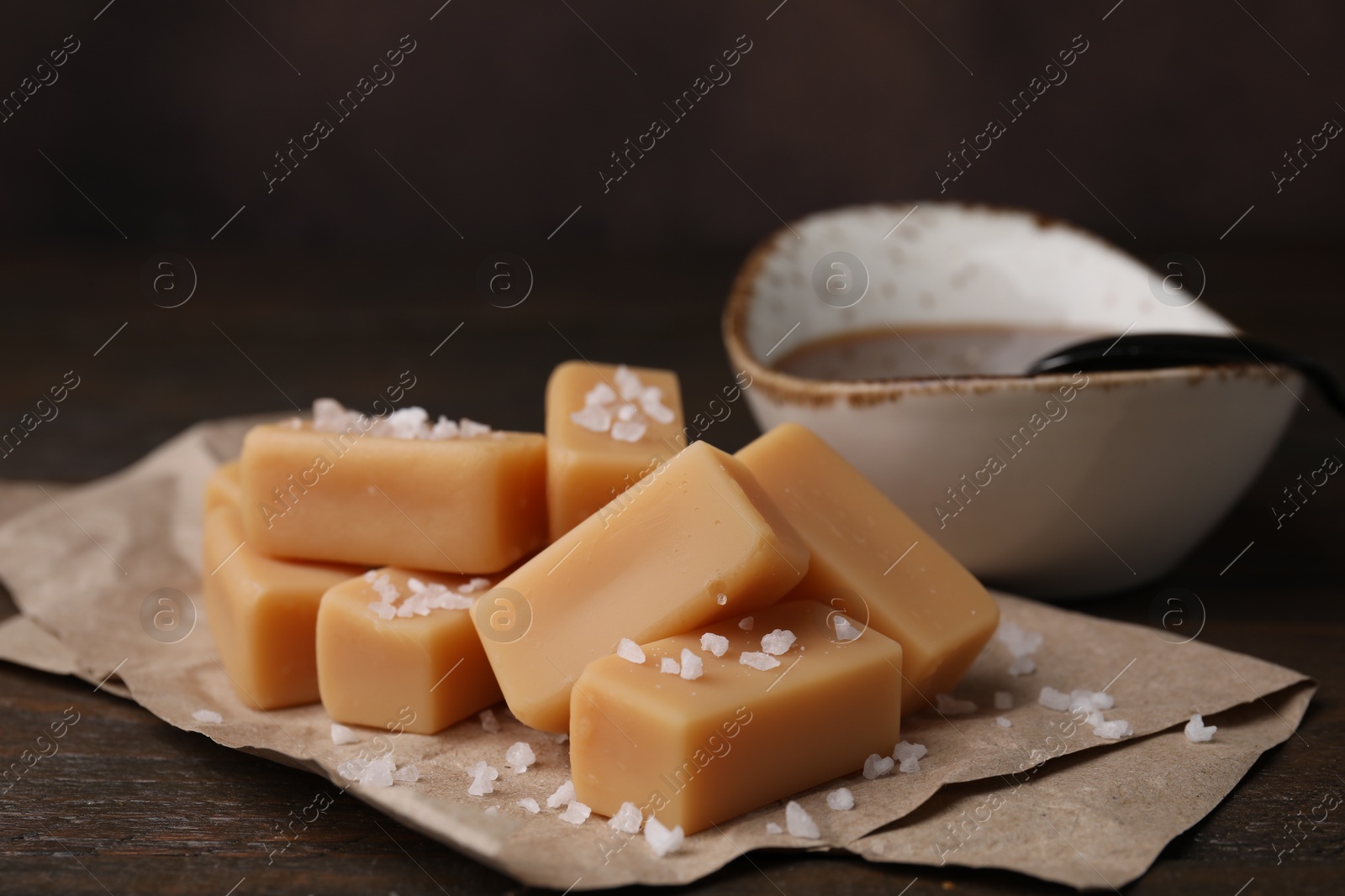 Photo of Delicious candies with sea salt and caramel sauce on wooden table, closeup