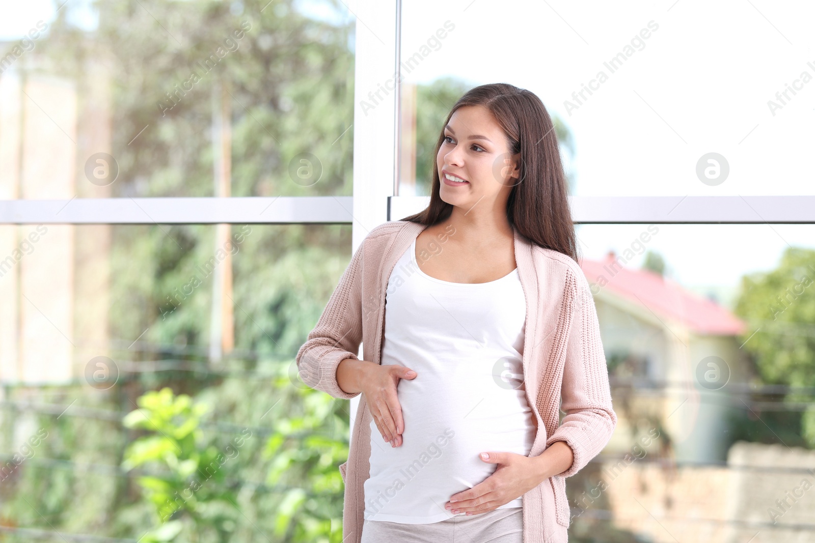 Photo of Happy pregnant woman standing near window at home