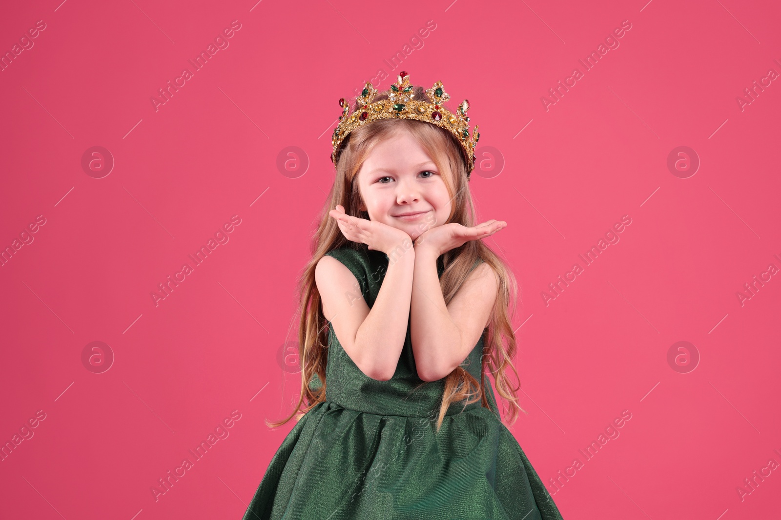 Photo of Cute girl in fairy dress and golden crown with gems on pink background. Little princess