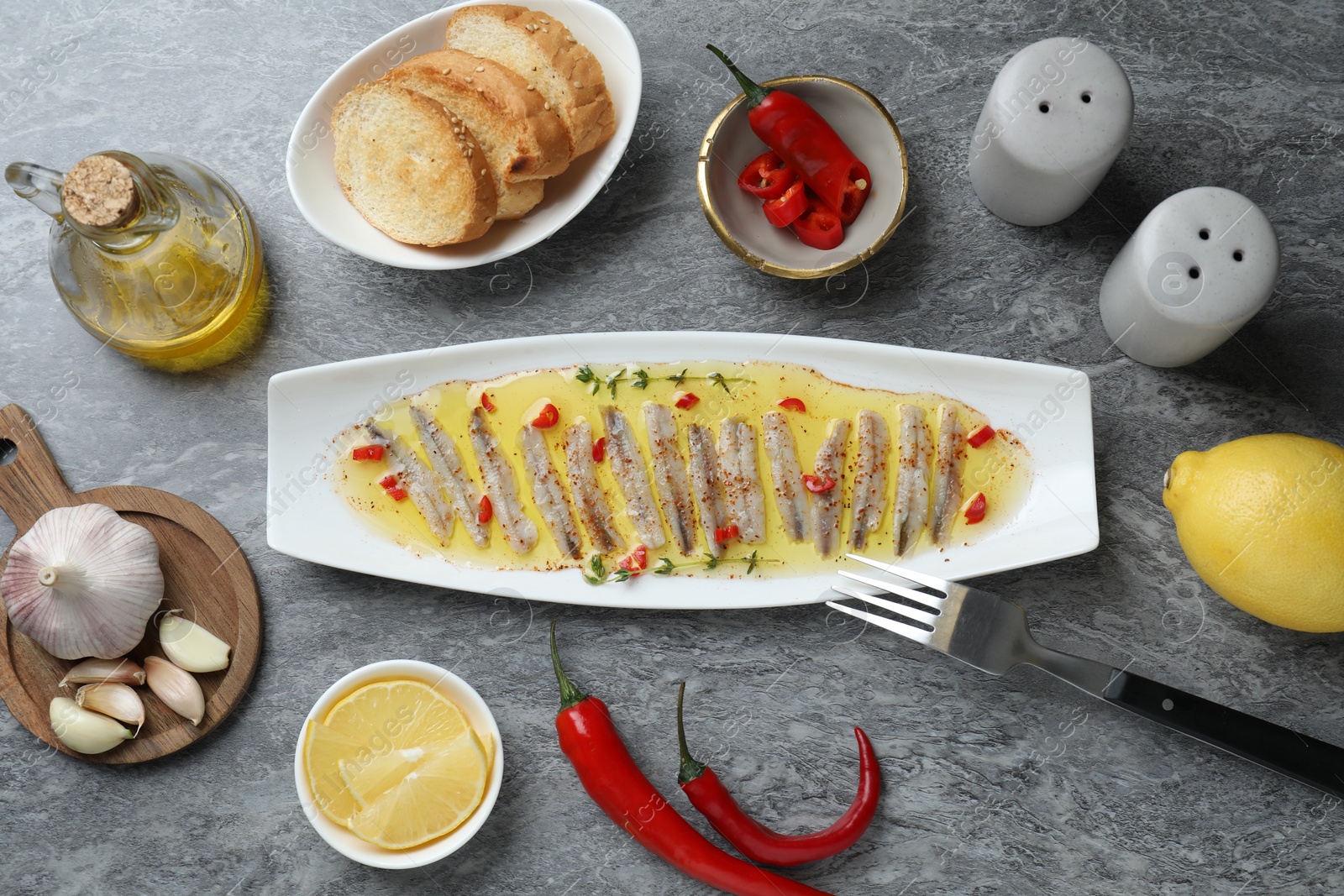 Photo of Tasty pickled anchovies with spices and products on gray table, flat lay