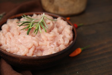 Fresh raw minced meat and rosemary in bowl on wooden table, closeup. Space for text