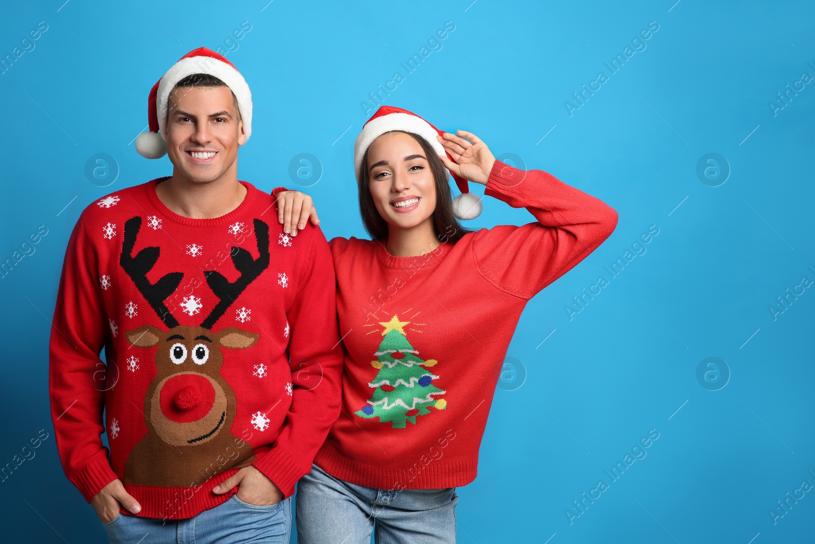 Photo of Couple in Christmas sweaters and Santa hats on blue background, space for text